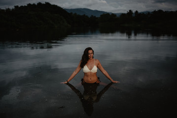 Young woman in swimwear standing in calm water of pond in evening in nature