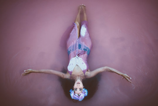 From above young and attractive long hair woman with wreath and wet dress lying in sea water