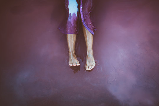 From above legs of graceful woman in wet blue dress sitting in sea water with sky reflection