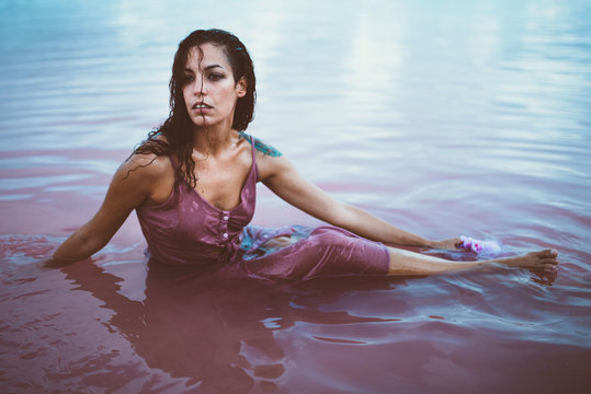 Young beautiful and fatal Hispanic woman with curly hair in wet summer dress sitting in sea water