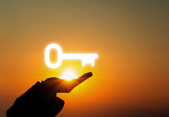 holding keys over the hand on sunset background, success concept 