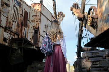 Fototapeta na wymiar beautiful young girl on the background of industrial landscape and old construction equipment. portrait in grunge style. the concept of loneliness and the world of technology.