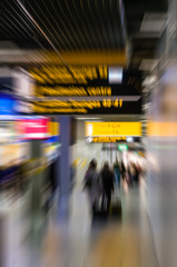 People walking towards the departure gates at an airport pulling suitcases, blurred to show movement and speed.