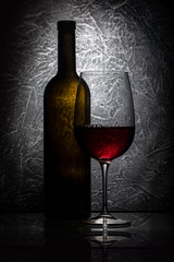 Red wine glass and wine bottle on gray stone background, drink against the wall in the old cellar
