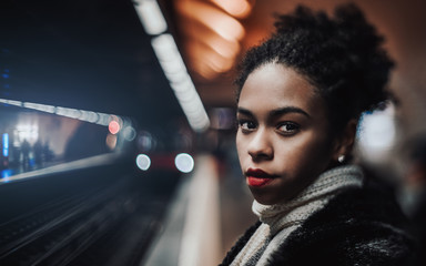 True tilt-shift portrait of a young African-American female on the platform with an arriving train...