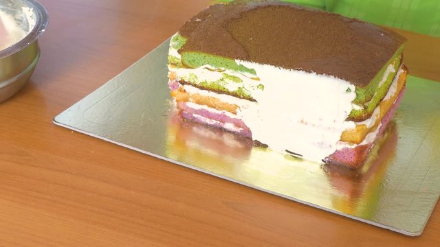 To grease with a cream with a special pastry knife of the side of a sponge cake with multi-colored cake layers