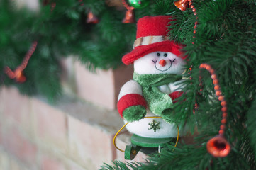 Christmas toy snowman, standing on the fireplace on the background of the Christmas tree