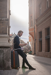 one man, traveler or tourist, resting on his suitcase while looking at a city map, on a street.