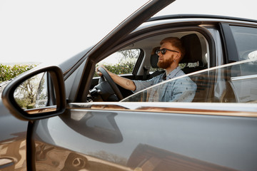 People, transportation, lifestyle and travel concept. Picture of handsome unshaven young European male driving gray automobile, looking at road with serious concentrated focused facial expression