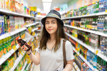 Cute young woman chooses a bottle of juice in the supermarket. Tint