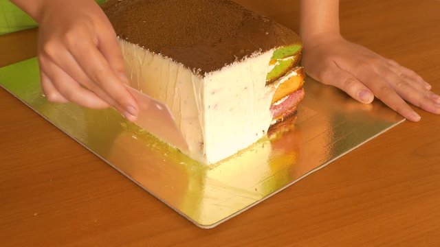 Lubricate butter cream with a special pastry knife on the side of a biscuit cake with multi-colored cake layers.