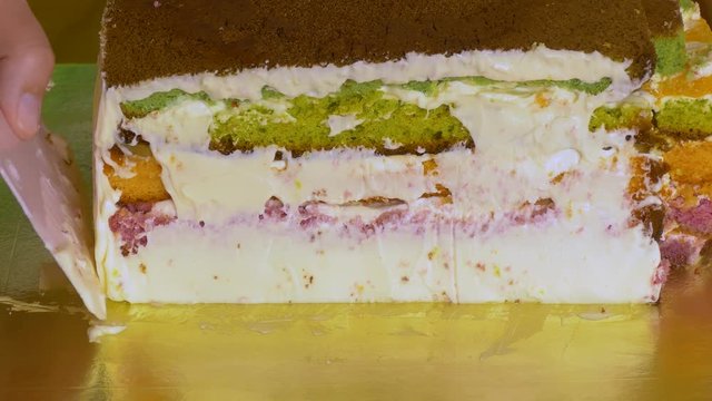 To grease with a cream with a special pastry knife of the side of a sponge cake with multi-colored cake layers