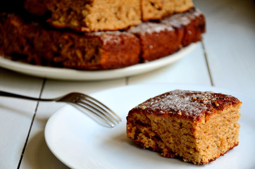 Cupcake on a white plate, with a fork, against the background of a stack of muffins on a white table ..