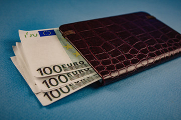 money in a leather wallet on a blue background.