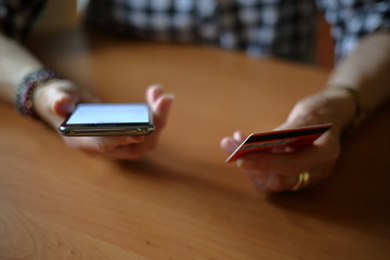 Senior woman buying paying on line with smart phone and credit card in hands, at wooden table, close up