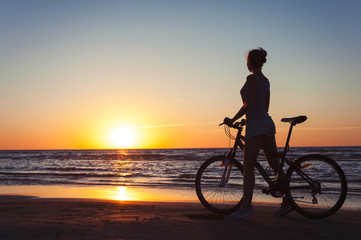 Fototapeta na wymiar Sporty woman cyclist silhouette on multicolored sunset background