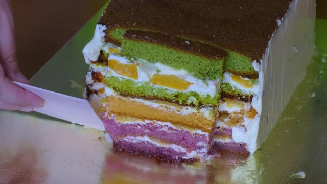 Lubricate butter cream with a special pastry knife on the side of a biscuit cake with multi-colored cake layers.