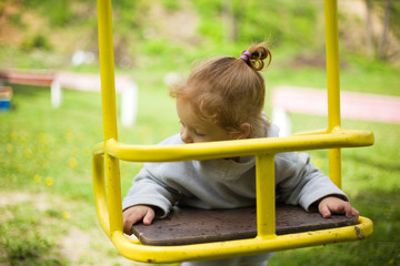 Obraz premium little beautiful red-haired girl hung on a swing, baby plays on a swing on the playground