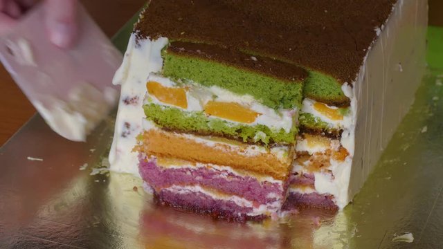 Lubricate butter cream with a special pastry knife on the side of a biscuit cake with multi-colored cake layers.