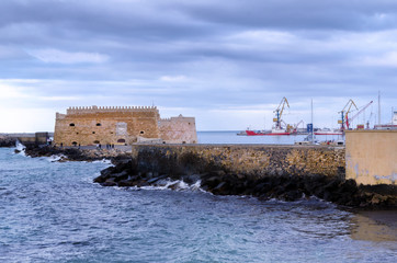 Fortress Koules, Crete - Greece. Fortress Koules (Castello a Mare) at the old Venetian port in Heraklion city at sunset time with cloudy sky. Big cranes visible in the background
