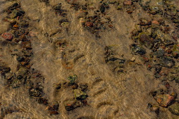 the sand and stones under water with the waves in the foreground .