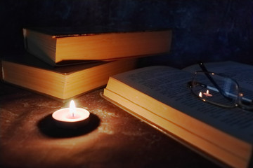 Lighted candles in an intimate setting, old books, yellowed from time to time, glasses in a knitted yellow thread.