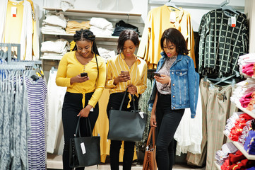 Three african woman at clothes store with new handbags. Shopping day. They look at mobile phones.