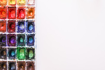 Watercolor paints, brushes and paper on white background. Flat lay, top view
