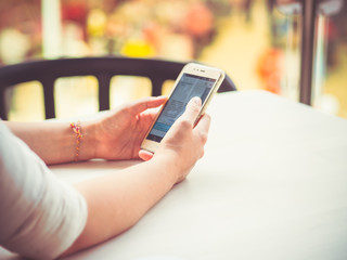 Closeup view of a young woman sitting in a cafe holding a smartphone in her hands for online communicating, paying, shopping.