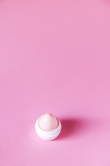 Lip balm in small white plastic container on soft pink background.