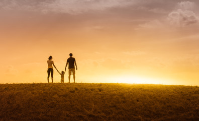 Family of three outdoors in the park holding hands facing sunset