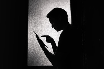 Silhouette of young man reading on tablet.