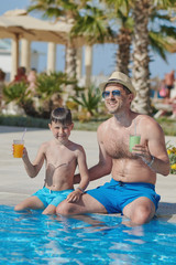 The portrait of European man and his son at the hotel’s swimming pool. They are drinking cocktails and enjoying their holidays.