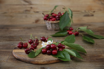  Fresh organic cherries on a branch with green leaves with cherries in a wicker basket with green leaves and white flowers on a wooden rustic background. The concept of healthy eating. With copy space