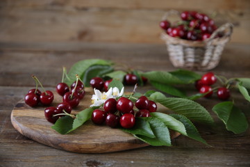  Fresh organic cherries on a branch with green leaves with cherries in a wicker basket with green leaves and white flowers on a wooden rustic background. The concept of healthy eating. With copy space