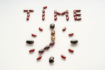 Word time and clock face shaped out of colorful kidney beans on white background. Healthy eating concept. Time to eat legumes