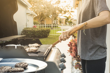 Backyard BBQ, person cooking steak, hamburger patties on a gas grill.