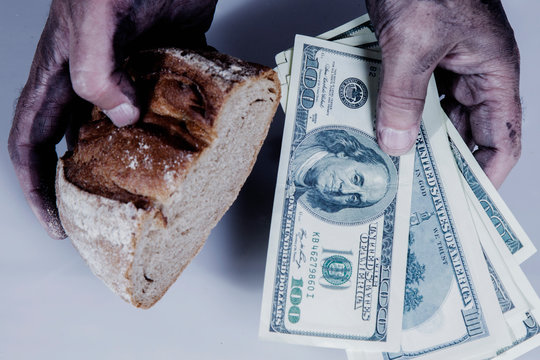 Close uo dirty hands of man with piece of bread and money as symbol of poverty, high cost of food.