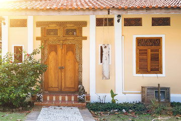 Entrance to the yellow house with wooden carved shutters. Old wooden door with carved patterns. Stone path leading to the stairs. Sunny day