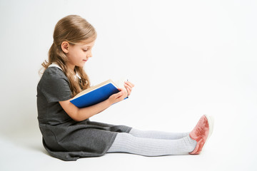 Little girl photographed against white background wearing school uniform dress isolated sitting with open blue book
