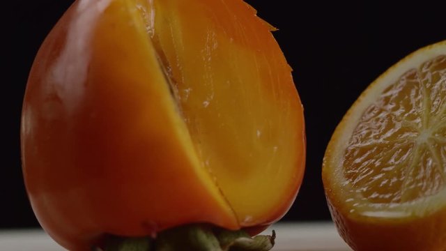 firstly we see a persimmon, then the picture moves from left to right and we see an orange cut into pieces, black background