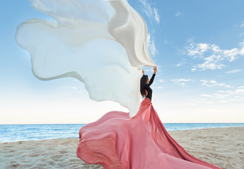 Slim Woman at the beach with long pink fabric. Sky background at the summer. Classic dancer on the...