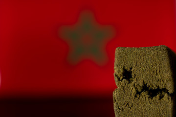 Medical Hashish in Kingdom of Morocco - CBD medical hashish from cannabis and Moroccan Flag on the black mirroring background.