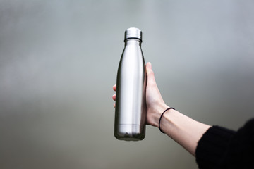 Close-up of steel thermo bottle in hand of young girl