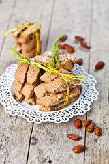 Fresh Italian cookies cantuccini stacked on white plate and almonds on ructic wooden table background.