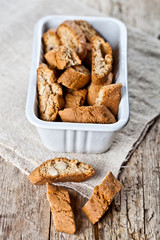 Italian cookies cantuccini in white ceramic bowl on linen napkin closeup on ructic wooden table background.