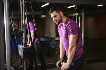 Young adult bodybuilder healthy fitness man doing triceps overhead extension rope exercise. Workout in public gym and sporty lifestyle concept