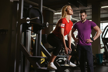 Young woman exercising workout with weight at the gym with male trainer instructor or coach in public gym fitness studio. Assistance sport healthy lifestyle concept