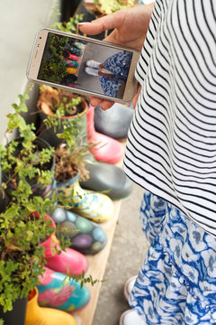 Closeup of a girl taking pictures on a smartphone multi-colored rubber boots as flower pots with different blooming flowers on the veranda