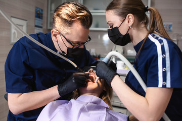 Mature dentist and his assistant working with the beatiful young female patient in a modern...